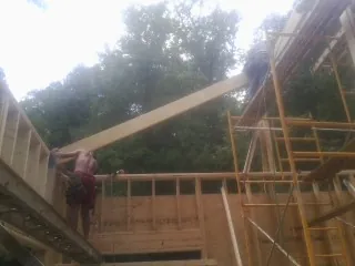 Carpenter raising a rafter beam on a new second story frame in Concord