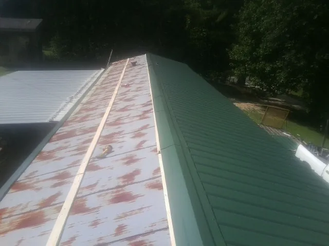 Old rusted panels beside newly installed green metal roofing — Wind Damage Roof Repair by Roofing Brothers in Concord