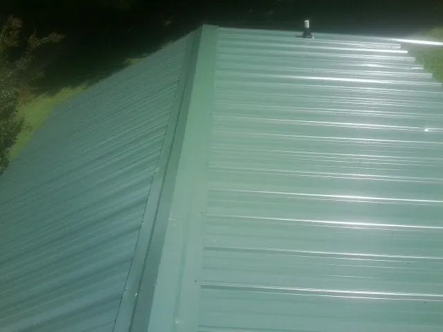 New green metal panels meeting at the ridge of a roof — Flat Roof Repair work by our crew in Concord