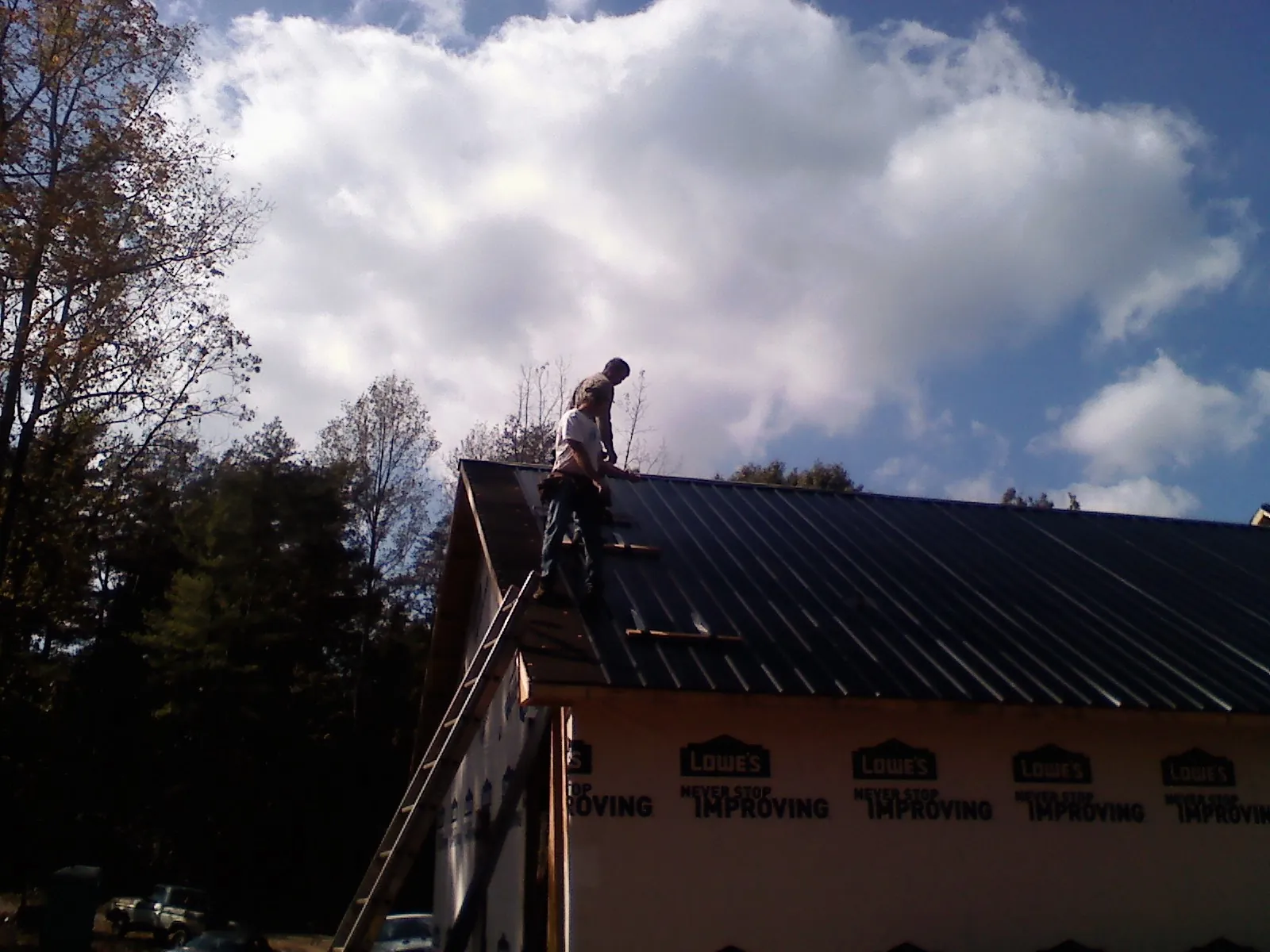 Roofer fastening dark metal panels high against a cloudy sky, from a Roof Inspection job in Concord